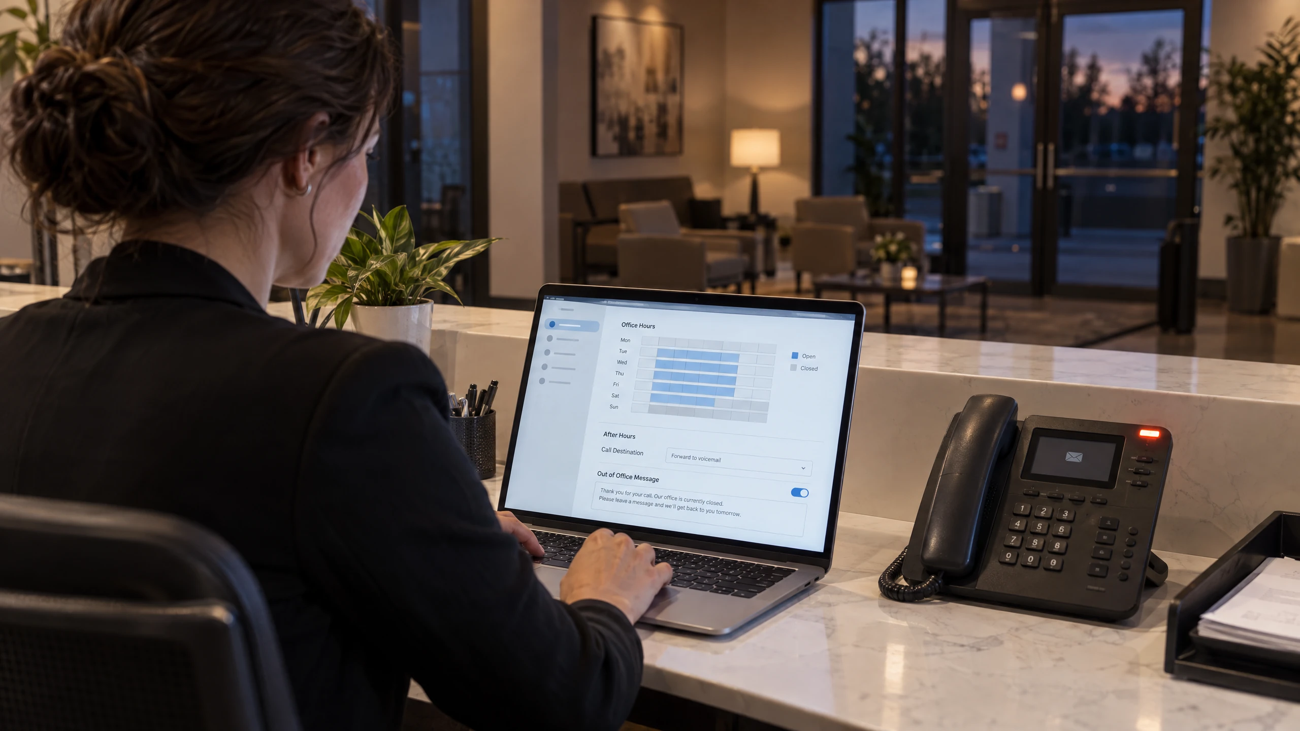 Office manager setting office hours and after-hours voicemail routing beside an IP desk phone (illustrative)